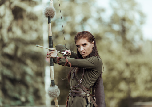 Young girl archery aiming at target, atmospheric photography with blurred background