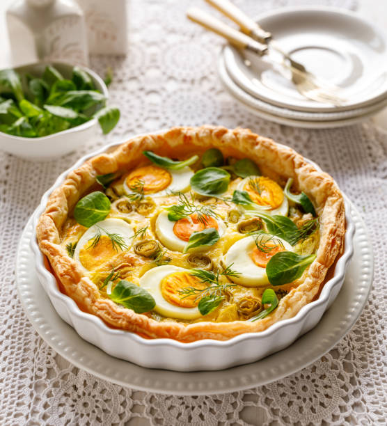 Quiche with with boiled eggs and leeks sprinkled with fresh lambs lettuce and dill served in casserole dish on a white table close up view