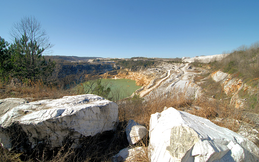 Aerial view of a mining quarry with heavy machinery, surrounded by forest.