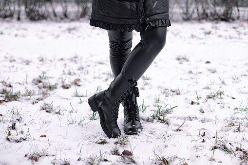 Female legs in fashion and stylish black boots on winter frozen grass background