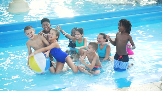 Children in pool reaching up to catch a beach ball