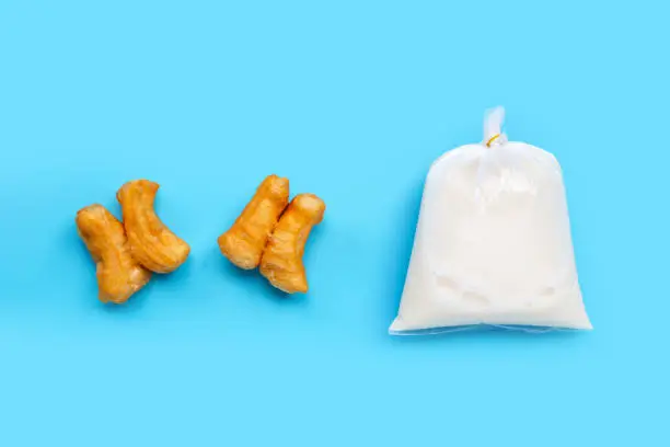 Soymilk in plastic bag with deep-fried dough stick or chinese bread stick on blue background. Top view