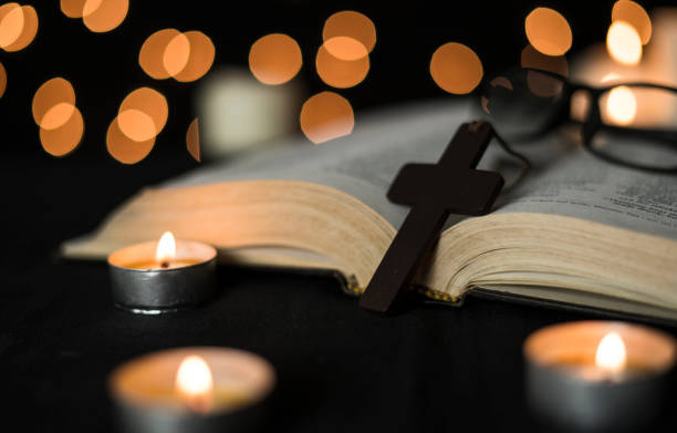 istock Cross with open bible with candles against bokeh lights background at night 1294236599