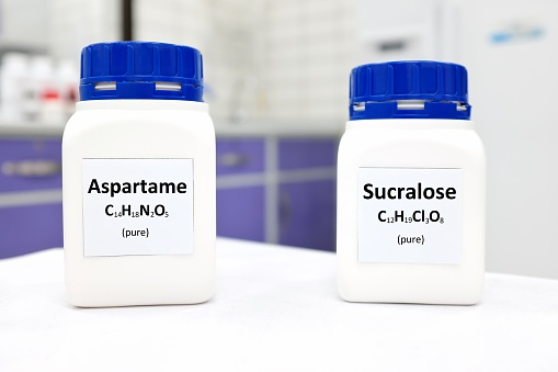 Selective focus of a bottle of pure aspartame and sucralose artificial sweetener sugar substitute chemical compound comparison. White laboratory background with copy space.