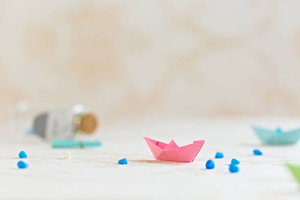 istock Pink paper boat on table, handicraft, blurry wishing bottle background, copy space 1294240461