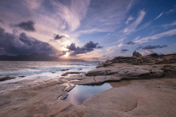 Waves washing onto the rocky coastline at Punta Caldanu near Lumio in the Balagne region of Corsica with the citadel of Calvi in the distance