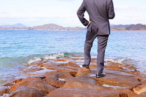 A businessman is standing on a rock.