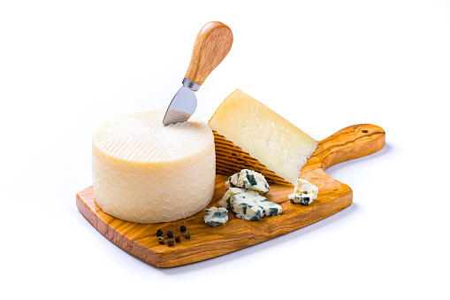 High angle view of a wooden cutting board with various kinds of cheese and a cheese knife isolated on white background. Studio shot taken with Canon EOS 6D Mark II and Canon EF 100 mm f/ 2.8