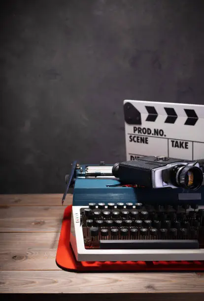 Photo of old vintage typewriter, camera and movie clapper board at wooden table near wall background surface, abstract retro writer concept