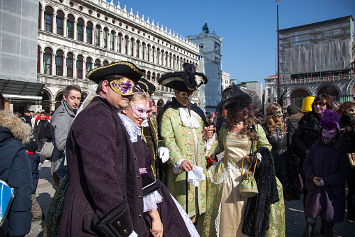 People with masks at the annual carnival in Venice walking among crowds of people, photographers, and tourists.