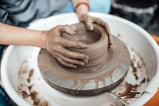 Female artist sculptor or potter making clay pottery on a spin wheel.