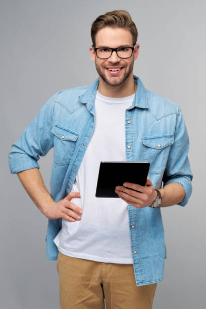 istock Happy young man wearing jeans shirt standing and using tablet over studio grey background 1294266524