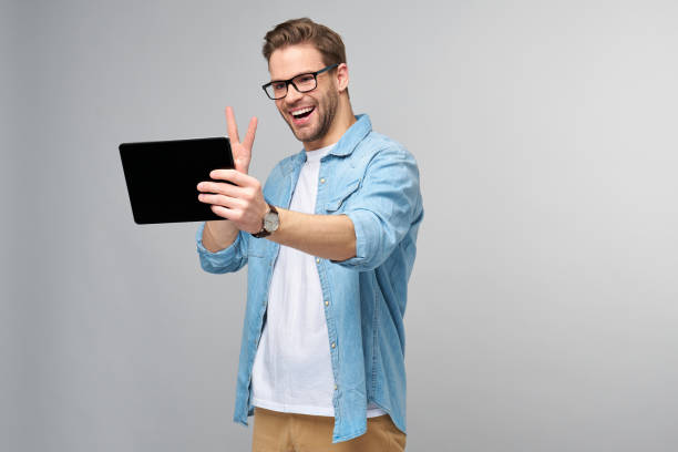 istock Happy young man wearing jeans shirt standing and using tablet over studio grey background 1294266535