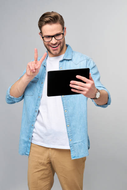 istock Happy young man wearing jeans shirt standing and using tablet over studio grey background 1294266538