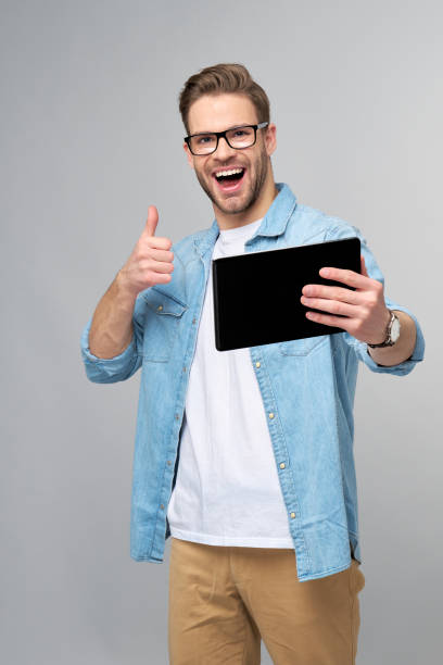 istock Happy young man wearing jeans shirt standing and using tablet over studio grey background 1294266541
