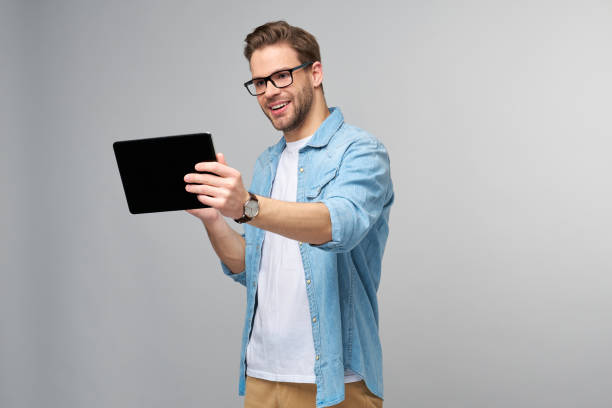 istock Happy young man wearing jeans shirt standing and using tablet over studio grey background 1294266546