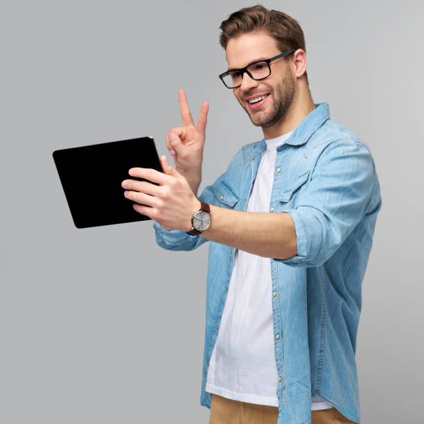 istock Happy young man wearing jeans shirt standing and using tablet over studio grey background 1294266548