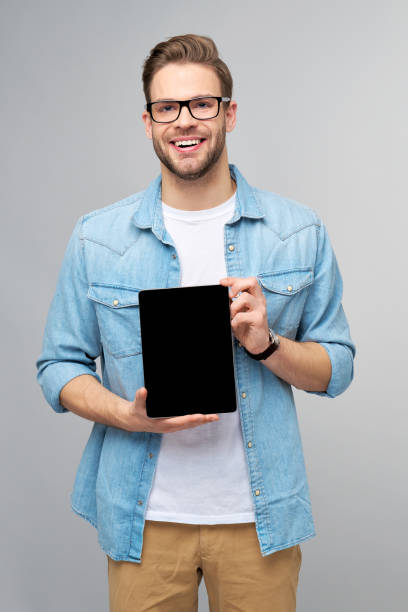 istock Happy young man wearing jeans shirt standing and holding tablet pc pad over studio grey background 1294266563