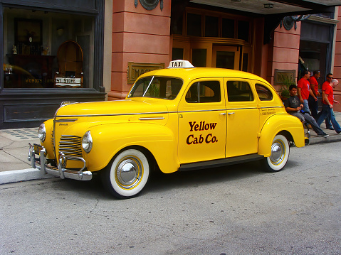 Orlando, Florida, United States of America (USA) - 08th August 2018: A german photographer visiting the Universal Film Studios, exploring a film set with a historical yellow cab.
