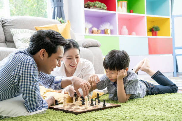 temps avec un concept aimé, famille asiatique heureuse jouant au jeu d’échecs dans le salon ensemble. - jeu déchecs photos et images de collection