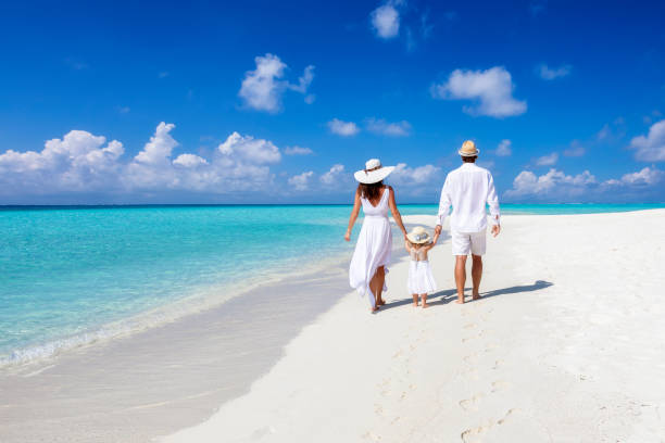 A beautiful family walks together on a tropical paradise beach in the Maldives A beautiful family walks together on a tropical paradise beach in the Maldives with turquoise ocean and white sand during their vacation time tourist resort photos stock pictures, royalty-free photos & images