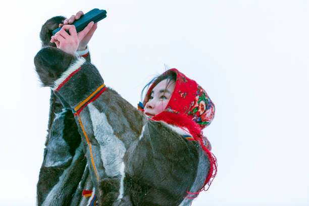 en ung flicka, i de nationella vinterkläderna i de norra invånarna i tundran, tar en selfie på en smartphone - same direction bildbanksfoton och bilder
