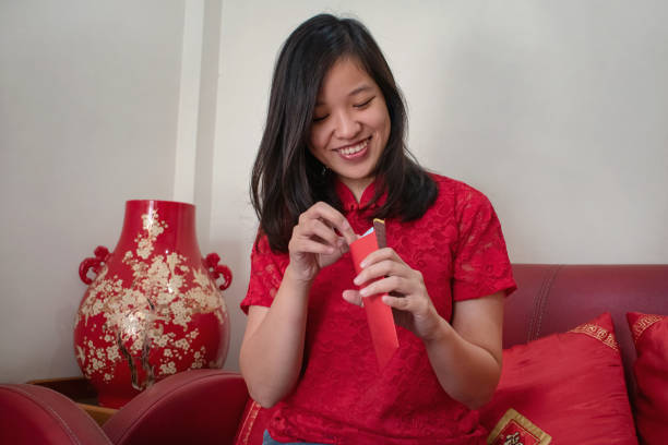 allegra giovane donna indonesiana cinese che guarda dentro la sua busta rossa - cheongsam chinese culture indoors looking at camera foto e immagini stock