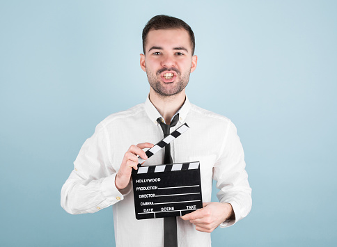 Professional male actor ready for shooting film, holds movie clapper, isolated on blue background.