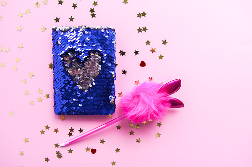 Bright composition of fashion accessories. Glitter sequins purse, notepad, funny pen and decorative tinsel. Different objects on soft pastel background. Flat lay, top view.