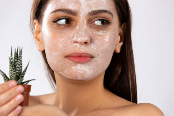 확대 된 사진. 그녀의 얼굴에 흰색 얼굴 마스크를 가진 백인 소녀와 손에 녹색 선인장. - clear sky human skin towel spa treatment 뉴스 사진 이미지