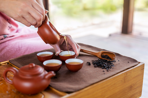 Brewing tea in traditional chinese teaware, Teapot in the hands of a girl pouring green tea into beautiful chinese cups close-up