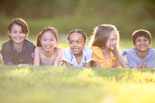 A multi ethnic group of children is laying down on the grass and enjoying their play time outside on a summer day.