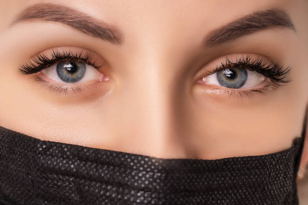 istock Eyelash Extension Procedure. Beautiful Woman with Extreme Long False Eyelashes. Makeup, Cosmetics. Beauty, Skincare. Woman in medical mask 1294303613