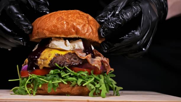 istock Craft burger is cooking on black background. Consist: sauce, arugula, tomato, onion, bacon, currant sauce, ricotta cheese, air bun and marble meat. 1294305038
