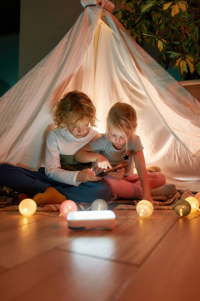 istock Two adorable little kids, brother and sister using tablet pc while sitting on a blanket in a teepee made with bedsheets at home 1294306145