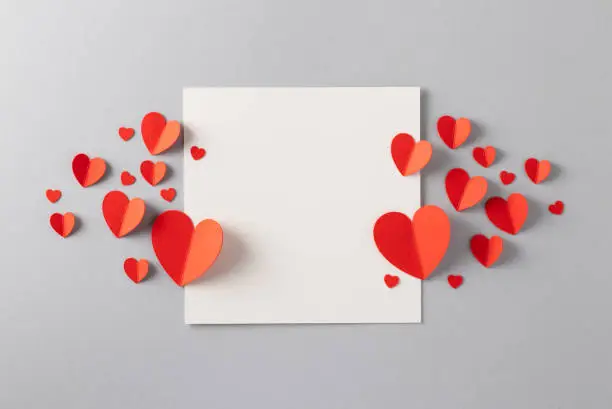 Photo of Red paper hearts with blank white note for Valentine’s Day message.