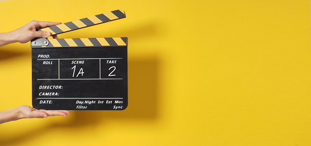 A Hand is holding Black clapper board or movie slate on yellow background.It has written a number.It is used in video production and movies, film industry on yellow background.