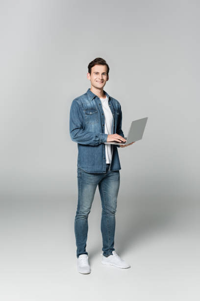 istock Cheerful man looking at camera while holding laptop on grey background 1294313812
