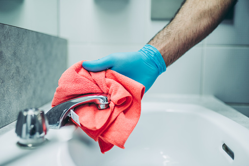 Hands of a janitor cleaning the  bathroom faucet. He is making sure everting is disinfected to be safe for use.