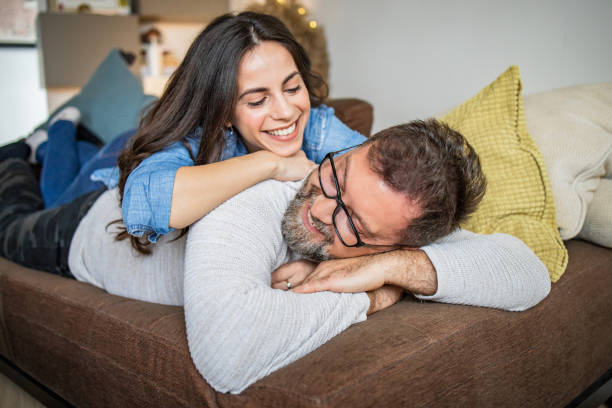 Loving couple relaxing on the couch at home Photo of happy couple relaxing at home. They are laying on the couch and smiling age contrast stock pictures, royalty-free photos & images
