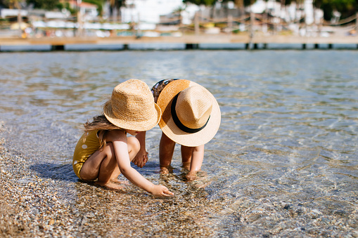 Happy sisters walking inside water during summer time - Kids having fun playing on the beach - Family love and travel vacation lifestyle concept