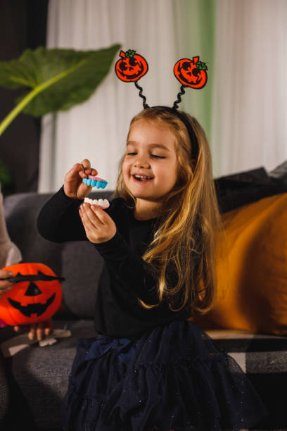 mała dziewczynka bawiąca się cukierkami halloweenowymi w kształcie zębów - house halloween autumn candid zdjęcia i obrazy z banku zdjęć