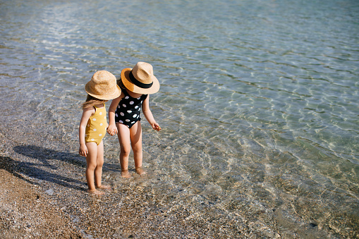 Happy sisters walking inside water during summer time - Kids having fun playing on the beach - Family love and travel vacation lifestyle concept