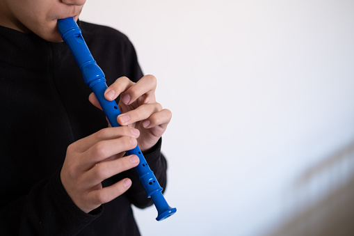 Young boy playing blue flute at home on white background