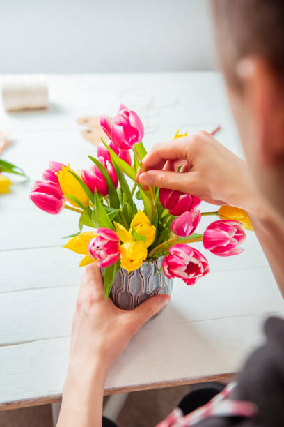 istock No face young man making spring bouquet using tulips. Online self-education of floristry. Learning flower arranging. Flowers delivery. Male florist creating order. Selective focus. Vertical card. 1294319823