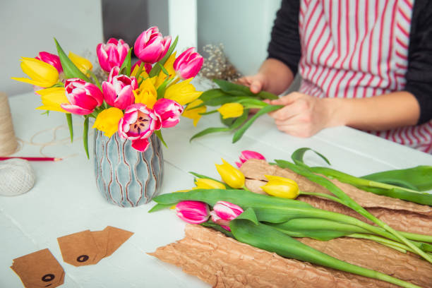 istock Focused Vase with flowers and blurred no face young man making spring bouquet using tulips. Online self-education of floristry. Learning flower arranging. Male florist creating order. Selective focus. 1294319824
