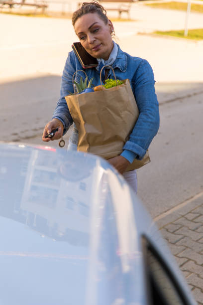 istock Phoning a friend while unlocking car trunk to load groceries 1294321241