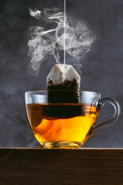 Glass of tea. Herbal tea bag and vapor on black background