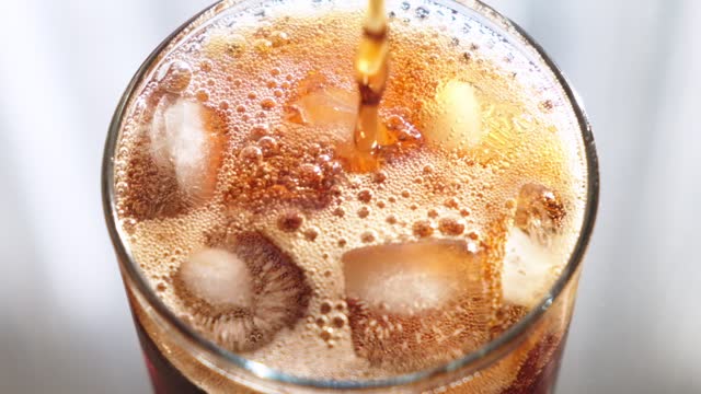 Top view close up footage of a glass with ice being filled with cola.