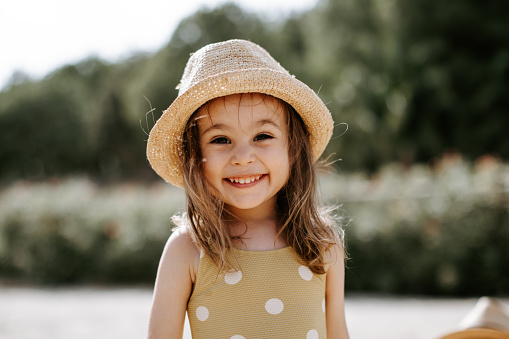 Portrait of a little girl laughing at the beach. The girl aged 3 is wearing a straw cowboy hat and has a long hair. Closeup portrait.